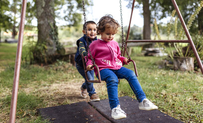 Zwei kleine Kinder spielen mit Schaukel in einem Garten - MGOF000812
