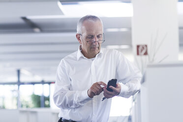 Businessman in open space office using smartphone - SGF001896