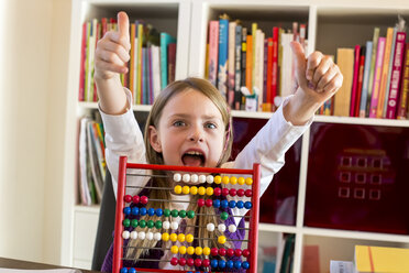 Portrait of cheering girl sitting behind abacus showing thumbs up - SARF002187