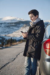 Teenage boy leaning on car, using smart phone - BZF000259