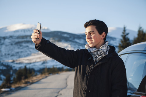 Jugendlicher lehnt sich an ein Auto und macht ein Selfie, lizenzfreies Stockfoto