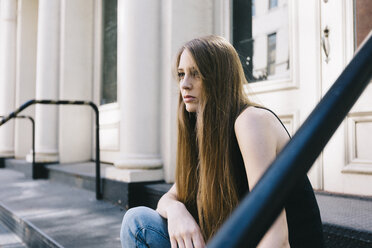USA, New York City, nachdenkliche junge Frau sitzt auf einer Treppe vor einer Eingangstür - GIOF000256
