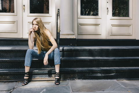 USA, New York City, pensive young woman sitting on stairs in front of an entry door stock photo