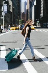 USA, New York City, junge Frau mit Rollkoffer beim Überqueren einer Straße - GIOF000261