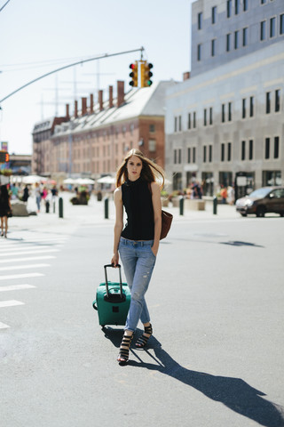 USA, New York City, junge Frau mit Rollkoffer steht auf einer Straße, lizenzfreies Stockfoto