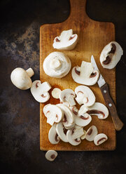 Whole and chopped champignons and kitchen knife on wooden board - KSWF001638