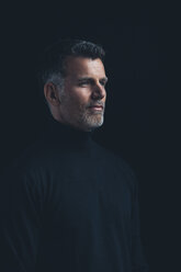 Portrait of man wearing black turtleneck in front of black background - CHAF001469