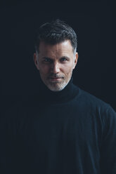 Portrait of man wearing black turtleneck in front of black background - CHAF001473