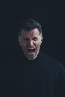 Porträt eines schreienden Mannes mit schwarzem Rollkragenpullover vor einem schwarzen Hintergrund - CHAF001475