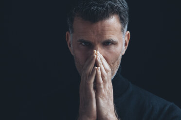 Porträt eines Mannes, der seinen Mund mit den Händen bedeckt, vor einem schwarzen Hintergrund - CHAF001477