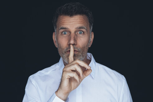 Porträt eines Mannes mit Finger auf dem Mund vor schwarzem Hintergrund - CHAF001482