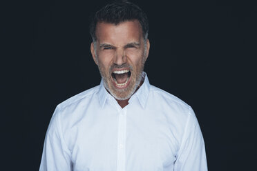 Porträt des schreienden Mannes weißes Hemd vor schwarzem Hintergrund - CHAF001484
