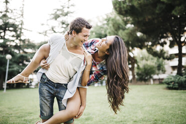 Young man giving his girlfriend a piggy back on a meadow in a park - JRFF000111