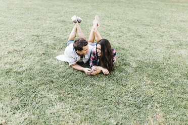 Young couple in love lying on a meadow in a park looking at each other - JRFF000112