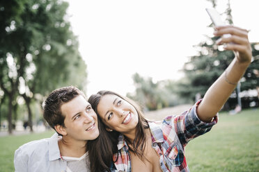 Porträt eines jungen verliebten Paares, das in einem Park ein Selfie mit seinem Smartphone macht - JRFF000121