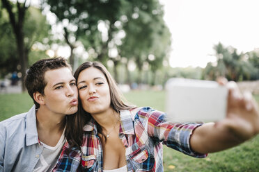 Porträt eines jungen verliebten Paares, das in einem Park ein Selfie mit seinem Smartphone macht - JRFF000126