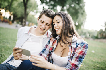 Porträt eines jungen verliebten Paares, das in einem Park etwas auf dem Smartphone beobachtet - JRFF000130