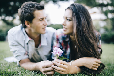 Young couple in love lying on a meadow in a park looking at each other - JRFF000131