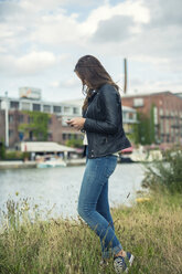 Deutschland, Münster, junge Frau auf einer Wiese in der Nähe des Stadthafens schaut auf ihr Smartphone - TAMF000277
