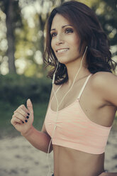 Portrait of smiling woman with earphones jogging - MFF002263
