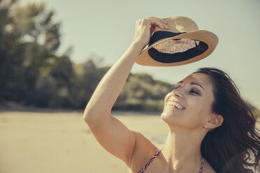 Porträt einer glücklichen Frau, die am Strand ihren Hut lüftet - MFF002272