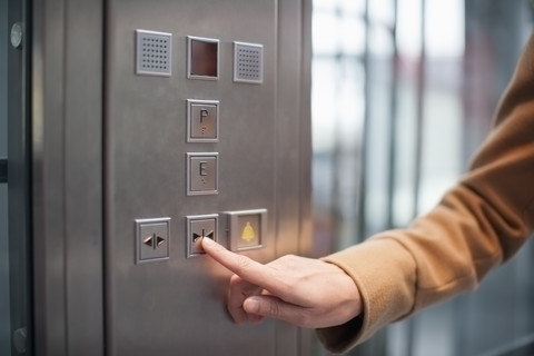 Frau drückt den Knopf eines Aufzugs, lizenzfreies Stockfoto