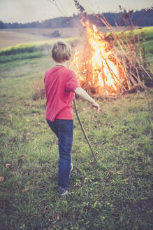 Rückenansicht eines Jungen, der ein Lagerfeuer auf einer Wiese beobachtet - SARF002196