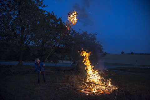 Deutschland, Junge am Lagerfeuer auf einer Wiese am Abend, lizenzfreies Stockfoto