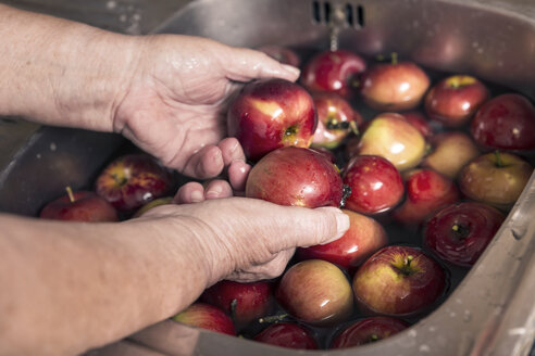 Senior woman cleaning apples in a sink, close-up - MIDF000686