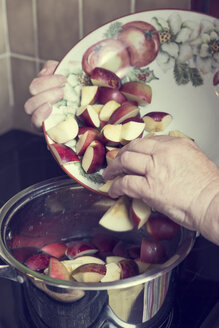 Ältere Frau legt Apfelstücke in einen Kochtopf für die Zubereitung von Apfelmus - MIDF000689