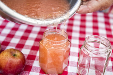 Ältere Frau gießt selbstgemachtes Apfelmus in ein Marmeladenglas, Nahaufnahme - MIDF000692