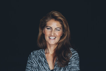 Portrait of twinkling woman with brown hair in front of black background - CHAF001499