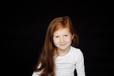 Portrait of redheaded smiling little girl in front of black background stock photo