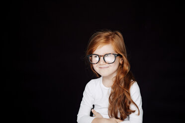 Portrait of redheaded smiling little girl wearing oversized glasses in front of black background - CHAF001530