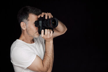 Mann beim Fotografieren mit Kamera vor schwarzem Hintergrund - CHAF001543