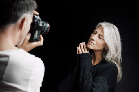 Mann fotografiert Frau vor schwarzem Hintergrund, lizenzfreies Stockfoto