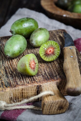 In Scheiben geschnittene und ganze Mini-Kiwis und ein Küchenmesser auf einem Holzschneidebrett - SBDF002300