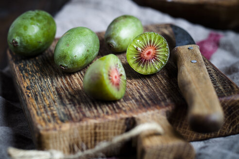 In Scheiben geschnittene und ganze Mini-Kiwis und Küchenmesser auf einem Holzschneidebrett - SBDF002301