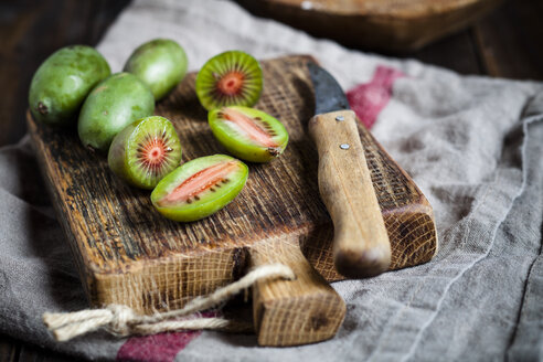 In Scheiben geschnittene und ganze Mini-Kiwis und ein Küchenmesser auf einem Holzschneidebrett - SBDF002302