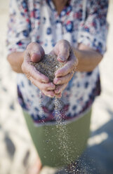 Die Hände einer älteren Frau halten Sand am Strand - RAEF000543