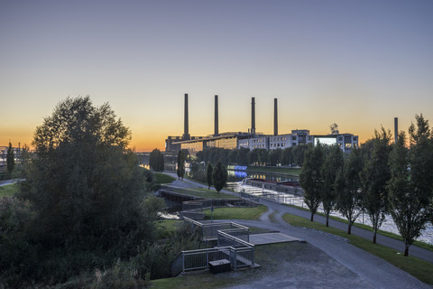 Deutschland, Niedersachsen, Wolfsburg, Blick auf die Autostadt am Abend, im Hintergrund das Blockheizkraftwerk von Volkswagen, lizenzfreies Stockfoto