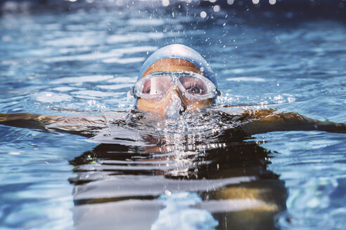 Weiblicher Triathlet mit Schwimmbrille, der im Schwimmbad aus dem Wasser sprudelt - MFF002321