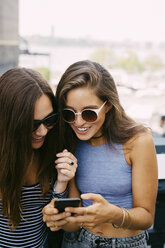USA, New York City, zwei lächelnde Freunde schauen auf ihr Handy - GIOF000279