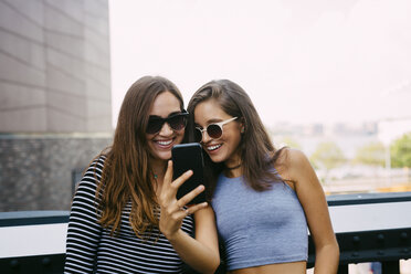 USA, New York City, two smiling friends looking at cell phone - GIOF000280