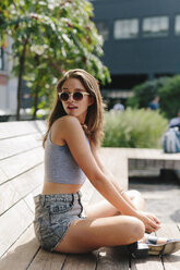 Brunette young woman wearing sunglasses relaxing on bench - GIOF000295