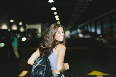 Smiling woman with a backpack ready to enter into a parking lot - GIOF000313