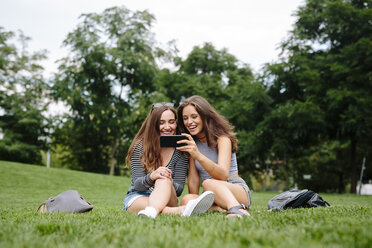 Zwei glückliche Freunde in einem Park schauen auf ihr Handy - GIOF000316