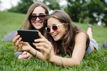 Zwei glückliche Freunde in einem Park schauen auf ihr Handy - GIOF000319
