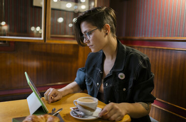 Junge Frau sitzt in einem Café und benutzt ein digitales Tablet - MGOF000845