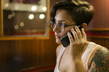 Tattooed young woman sitting in a coffee shop talking on phone - MGOF000852